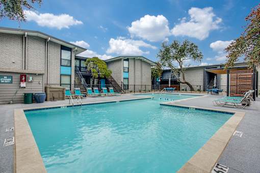 A large swimming pool in front of a building with a blue sky and clouds in the background.