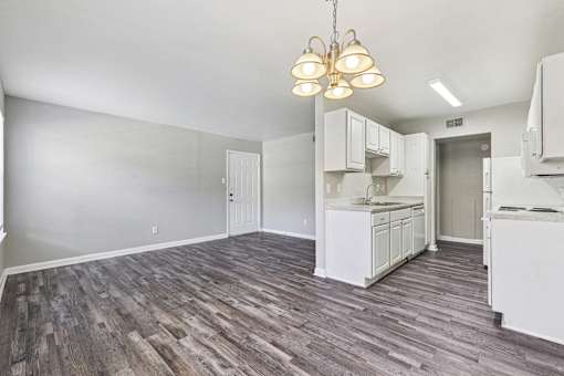 A kitchen area with white cabinets and a wooden floor.