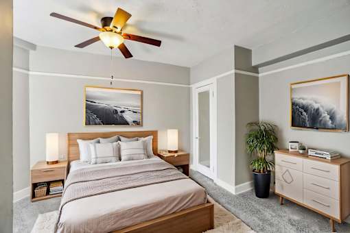 A bedroom with a large bed, a ceiling fan, and two framed pictures on the wall.
