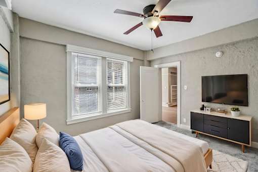 A bedroom with a bed, a ceiling fan, and a television.