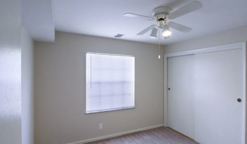 Bedroom with white walls, grey carpet, white closets, a large window, and a ceiling fan.