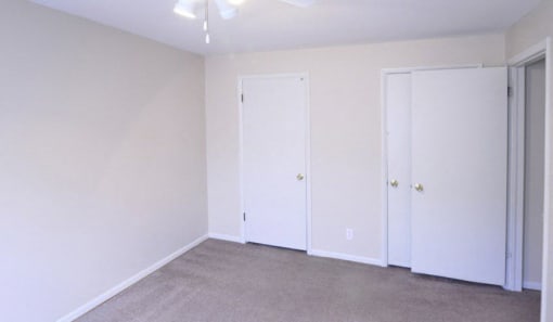 Bedroom with two closets, white walls, and grey carpet.