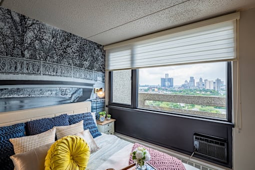 a bedroom with a bed and a window overlooking a city at City Club Apartments Lafayette Park, Detroit, Michigan