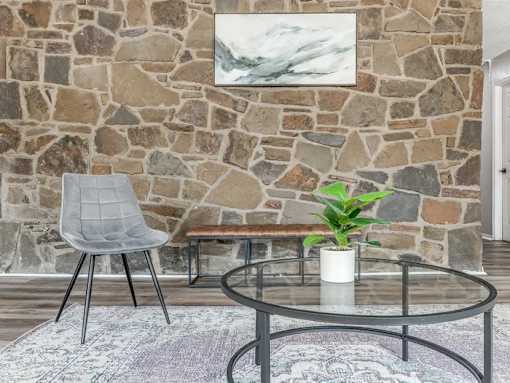 A grey chair sits in front of a stone wall with a plant on the table.