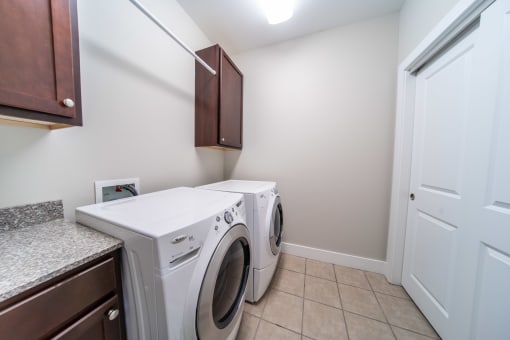 Laundry room with tile floors, washer and dryer, cabinets, and hanging rack.