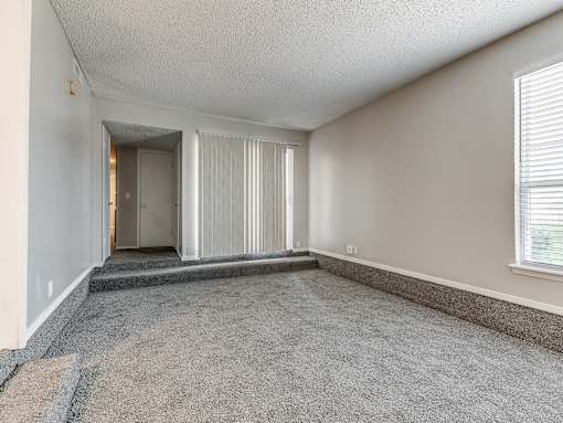 A room with a carpeted floor and a window with blinds.