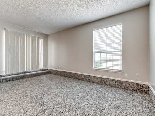 A room with a carpeted floor and a window with blinds.
