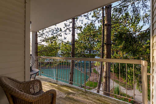 A balcony with a chair and a view of a pool and trees.