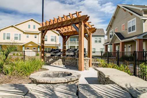 A wooden pergola is in the middle of a courtyard with a fire pit.