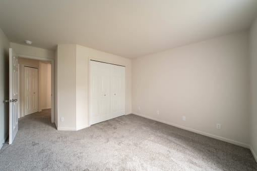 a bedroom with white walls and carpet and a door to a closet