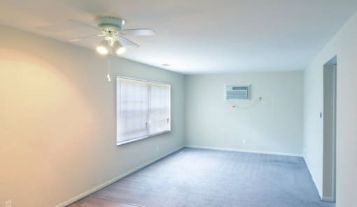 Living room with grey carpet, white walls, a large picture window and ceiling fan.