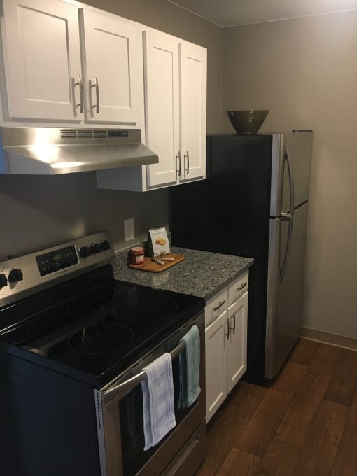 Kitchen with white cabinets, grey counter tops, hardwood like flooring, grey walls, and stainless steal stove and fridge.