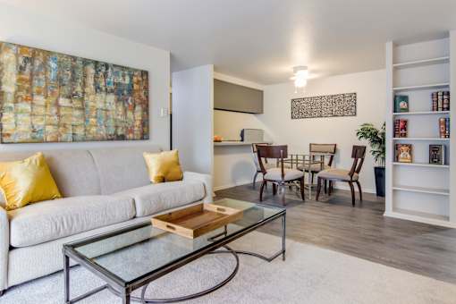 A living room with a white couch, a glass coffee table, and a painting on the wall.