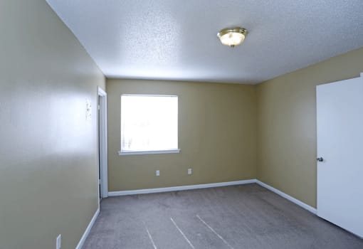 Empty carpeted bedroom with a large window.