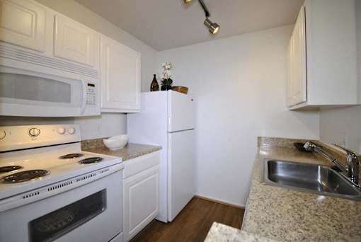 A white kitchen with a stove, microwave, refrigerator, and sink.