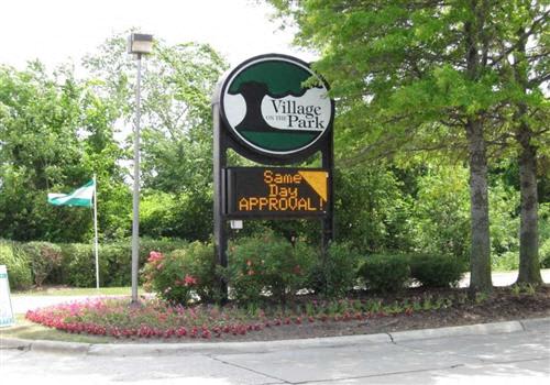 A sign for Village Park is displayed in front of a green bush.
