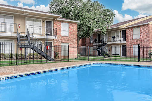 A swimming pool in front of a brick building with a black metal staircase.