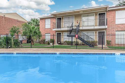 A swimming pool in front of a brick building with a black railing.