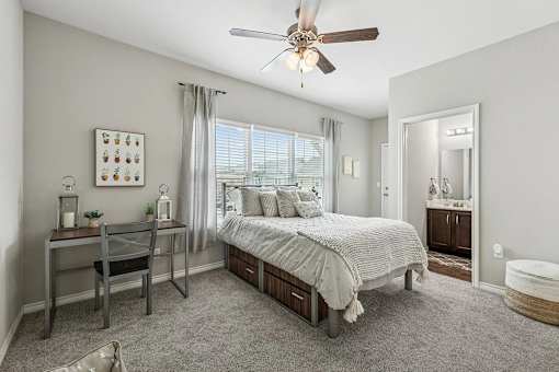 A bedroom with a bed, desk, chair, and a ceiling fan.