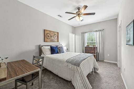 A bedroom with a bed, a table, and a ceiling fan.