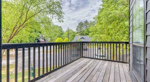 A wooden deck with a black railing and trees in the background.