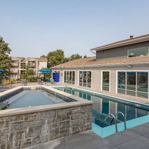 A swimming pool with a stone wall and a hot tub in the foreground.