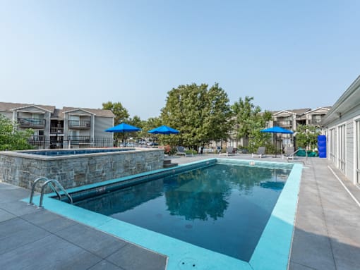 A swimming pool surrounded by a stone wall and blue umbrellas.