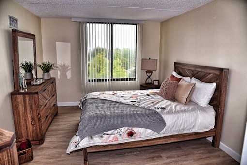A bedroom with a large bed, wooden dresser, and a window with blinds.