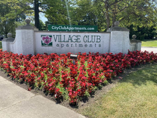 a sign for the village club apartments in front of a flower garden at Village Club on Franklin, Southfield, MI