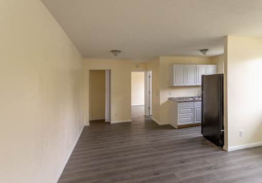 A kitchen area with a black refrigerator and wooden flooring.