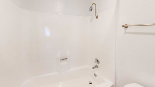 A white bathtub with a shower head and a towel bar.