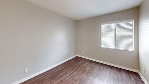 A room with wooden flooring and a window with blinds.