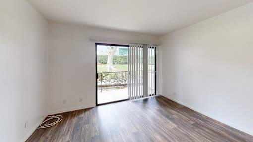 A room with wooden floors and white walls has a sliding glass door.