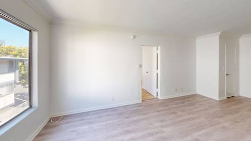 A room with white walls and wooden flooring, with a door on the right side.