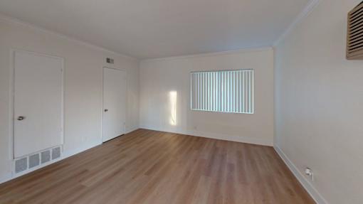 A room with wooden floors and white walls, with a window covered by vertical blinds.