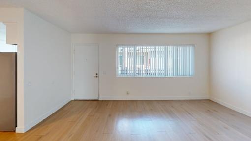 A room with a wooden floor and a window with blinds.