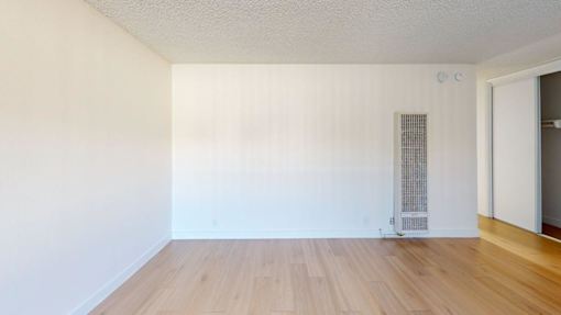 A room with a wooden floor and a white wall with a door on the right side.