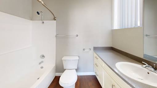 A white toilet is in a bathroom with a white tub and sink.