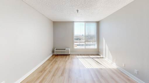 A room with wooden floors and white walls, with a window letting in natural light.