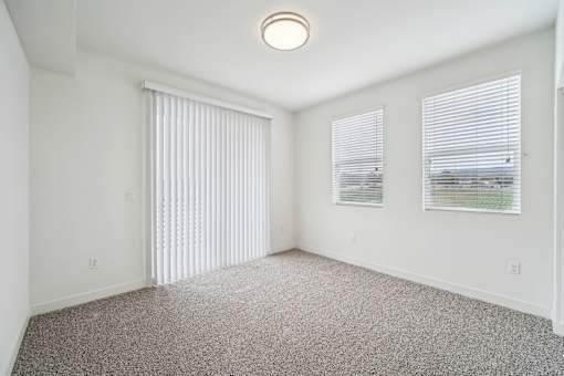 A room with a carpeted floor, a window with blinds, and a ceiling light.