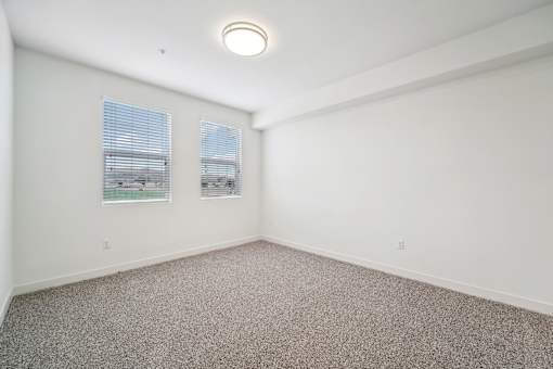 A room with a carpeted floor and two windows.