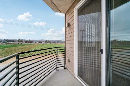 A balcony with a glass door and a metal railing overlooks a field.
