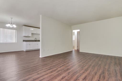 an empty living room with a kitchen in the background