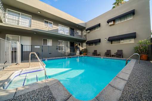A swimming pool in front of a building with a sunny day.