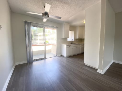 an empty living room with a sliding glass door to a kitchen