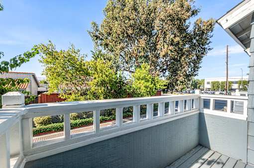 A balcony with a white railing and a view of trees and buildings.