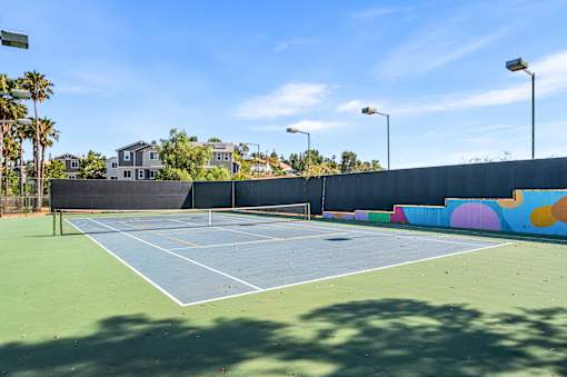 A tennis court with a blue surface and white lines, surrounded by a wall with colorful circles and a fence.