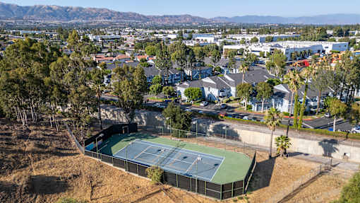 A tennis court is surrounded by houses and grass trees.