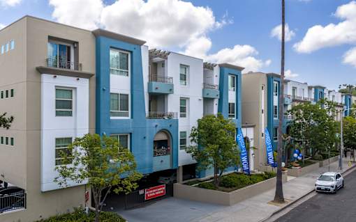 A row of modern apartment buildings with balconies and trees in front.