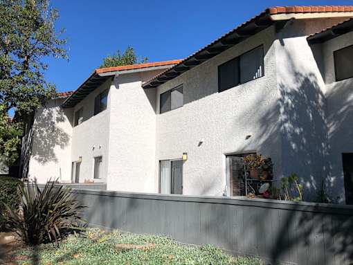 A white house with a red tile roof and a grey wall.
